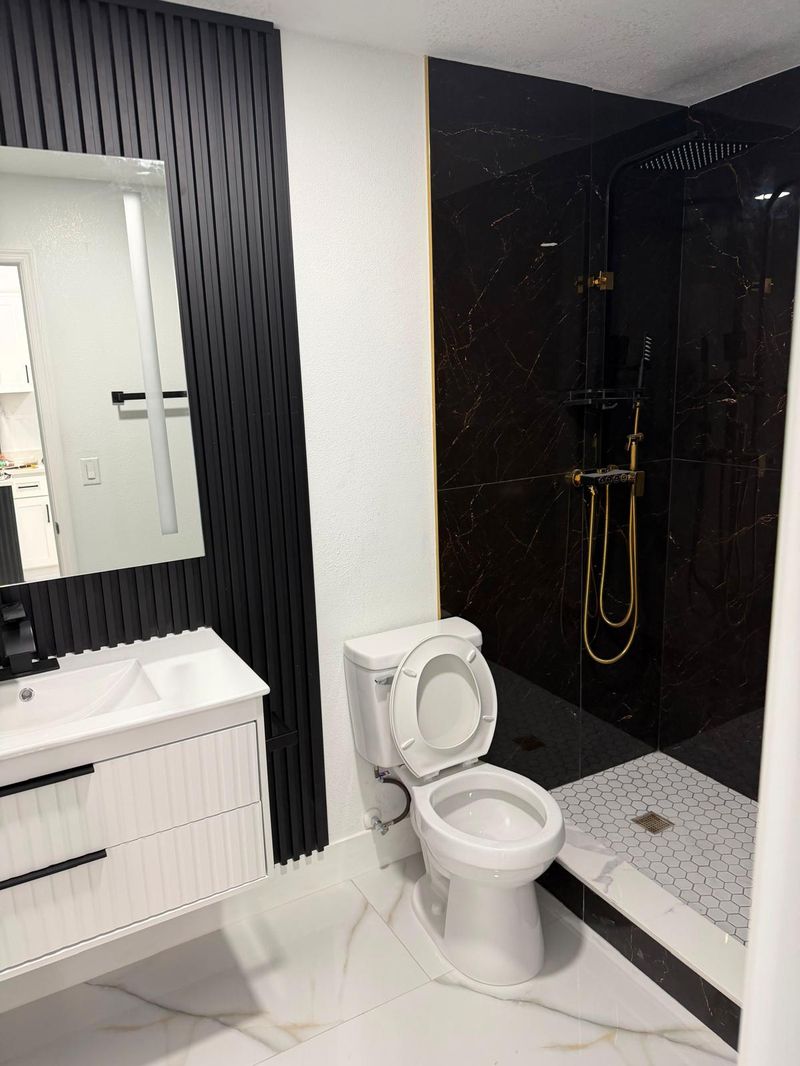 Baño remodelado con ducha de vidrio y pared negra