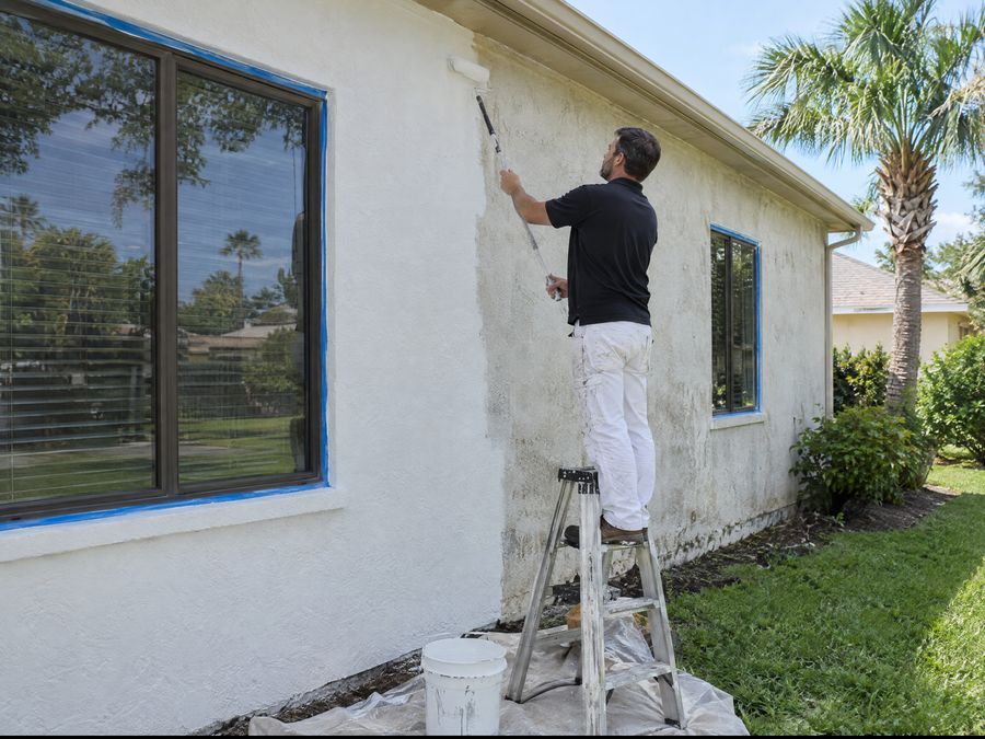 Pintor aplicando pintura blanca en la fachada de una casa